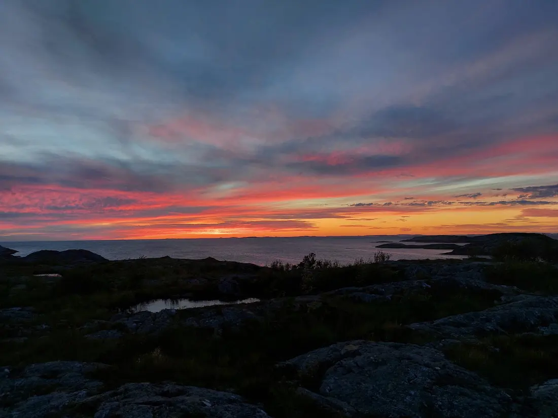 Dramatisk rød solnedgangshimmel over den steinete kysten av Otterøya