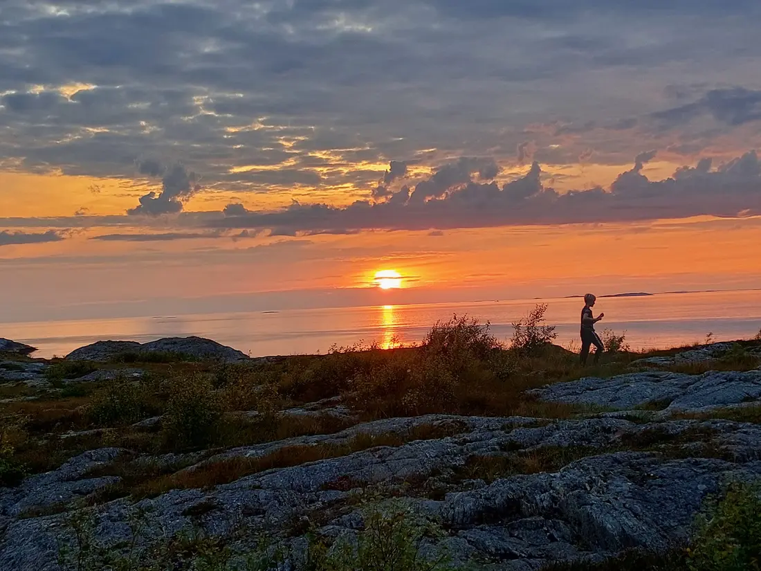 En person som går langs kystberg i solnedgang