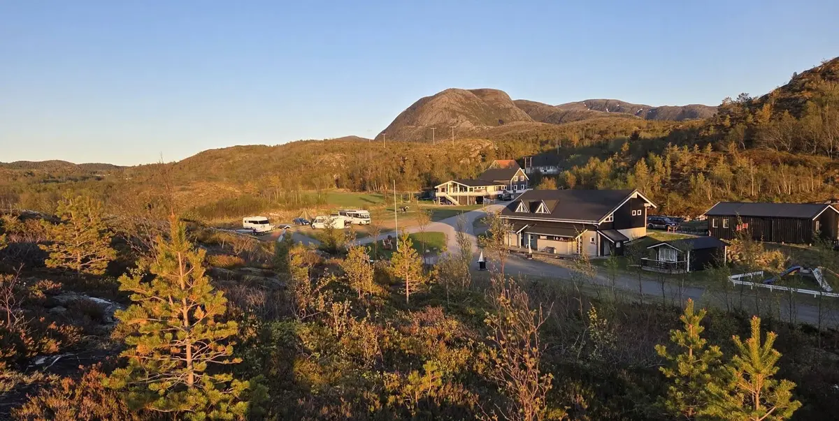 Gyllent kveldslys over resepsjonsbygget, hyttene og fjellene bak campingplassen