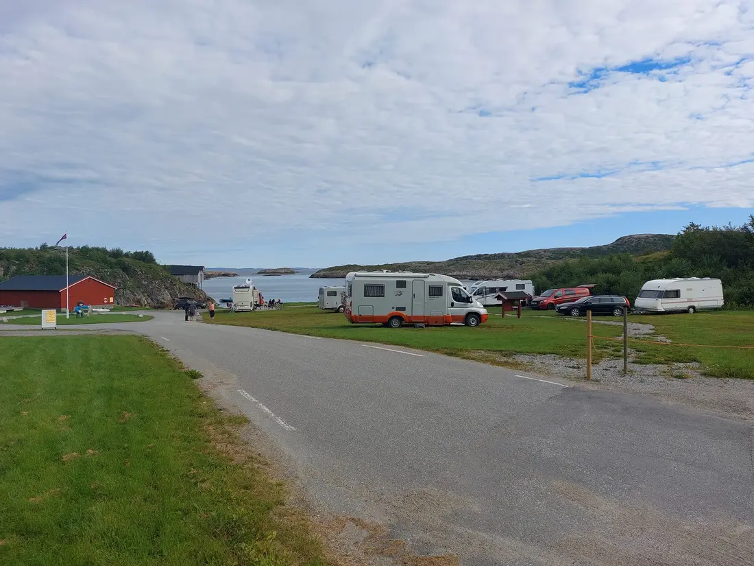 Bobiler og campingvogner parkert på en gressplass nær sjøen