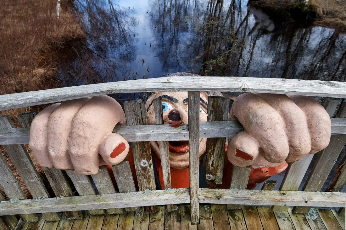 Trollfigur som strekker seg opp under ei trebru i trollparken